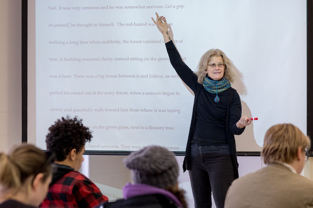 Professor gesturing at a screen with text on it while students in the foreground listen