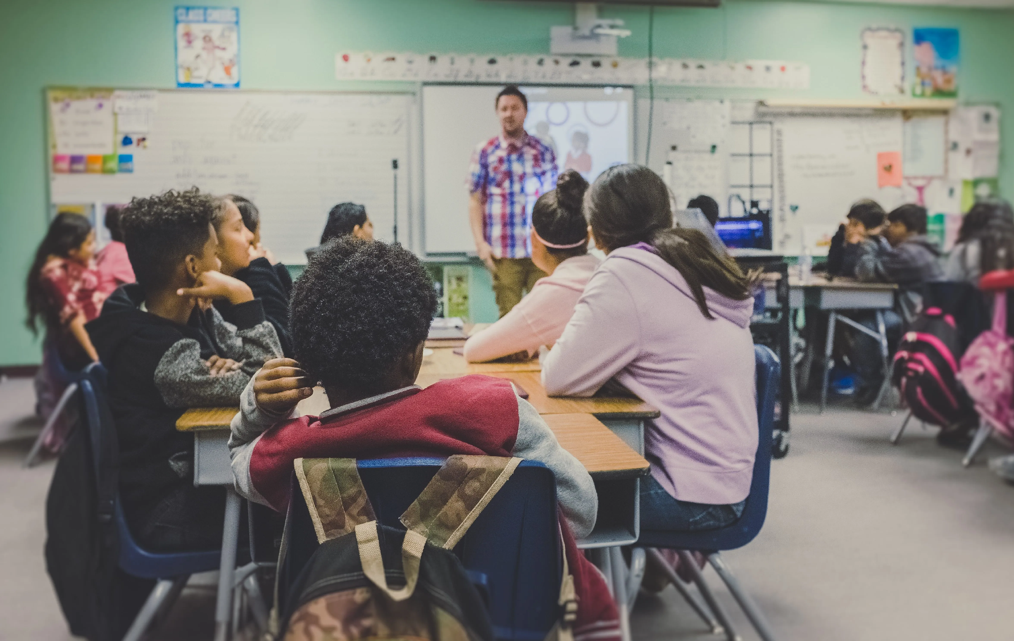 students in a classroom facing a teacher. students are early high school age